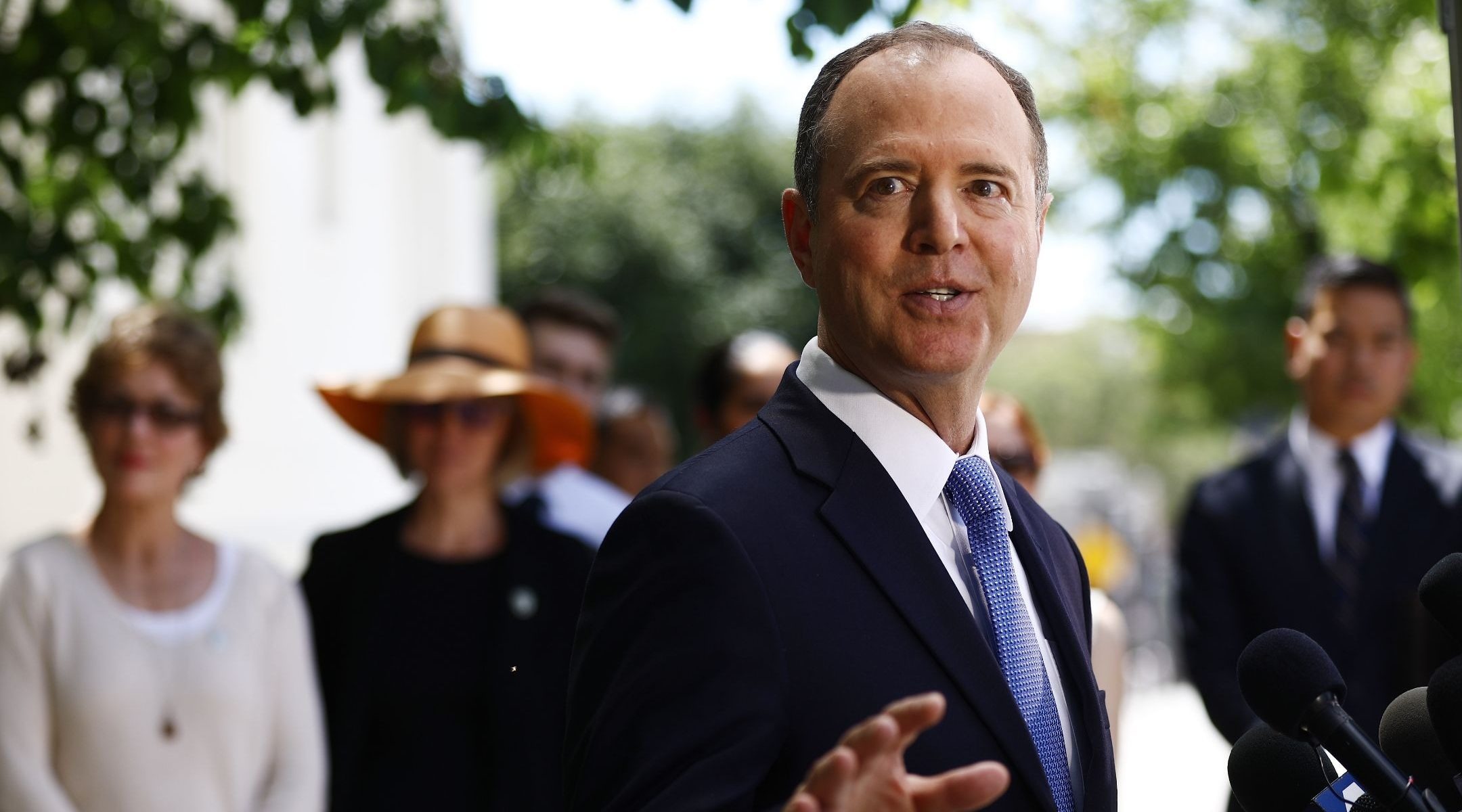 a man in a suit speaks before a small crowd outdoors