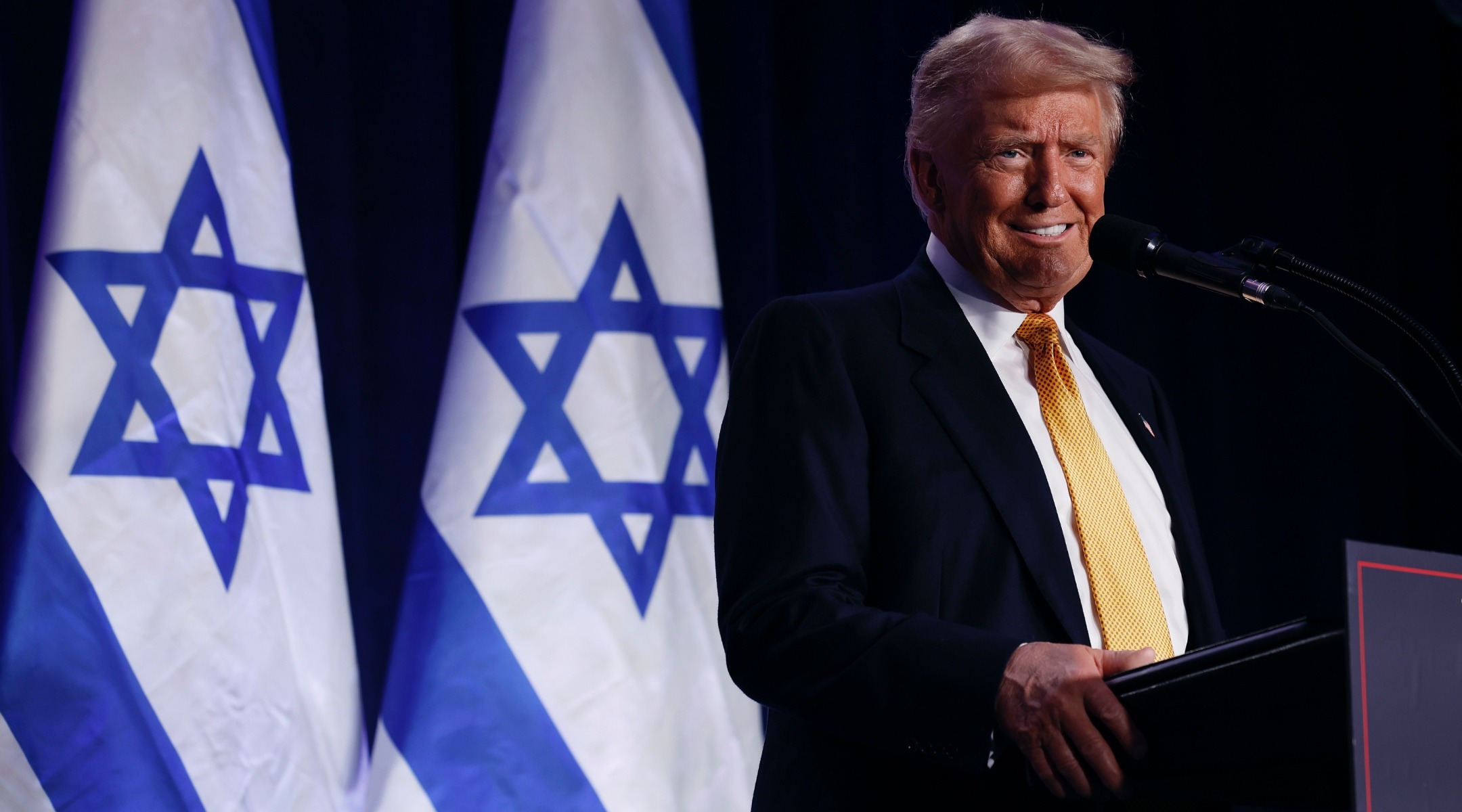 Trump speaks at a lectern in front of two Israeli flags