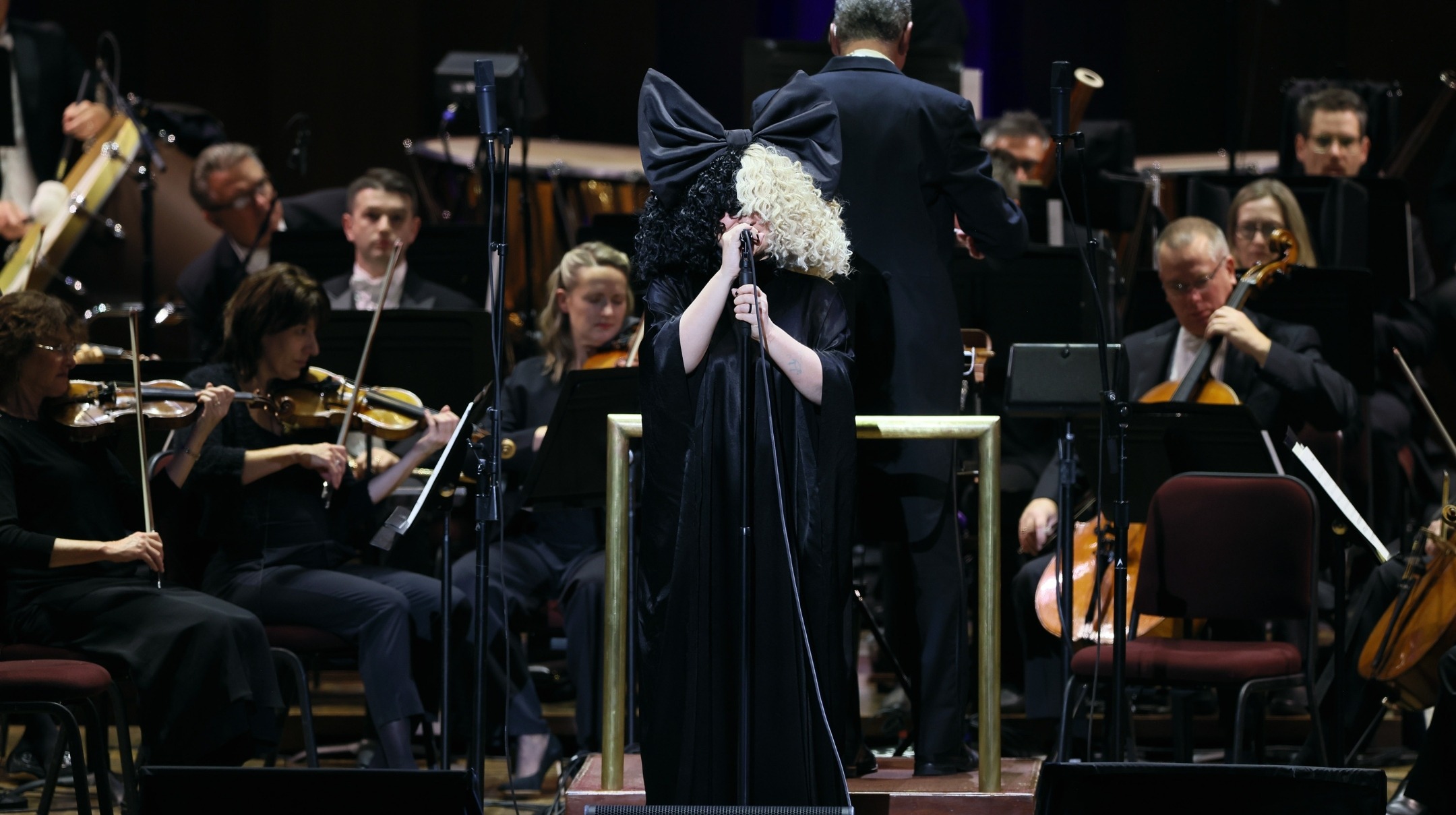 Sia, in her signature black and white wig, sings, backed by an orchestra
