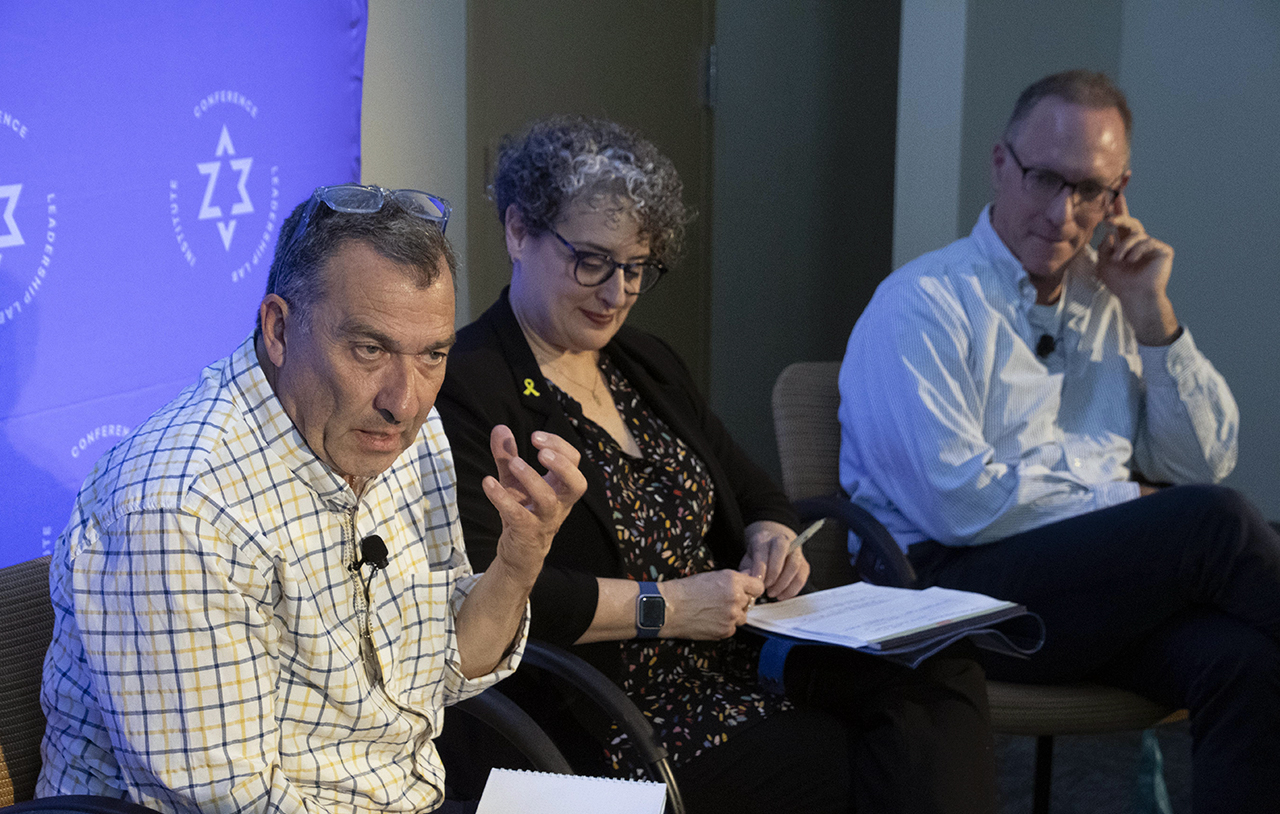 a man speaks. a woman and another man seated next to him look on.