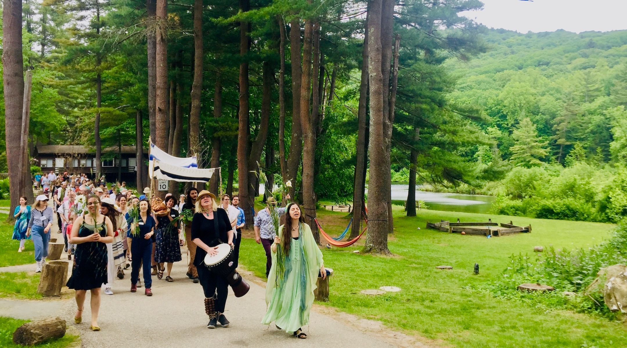 People parade through a forest, led by musicians with guitars and hand drums