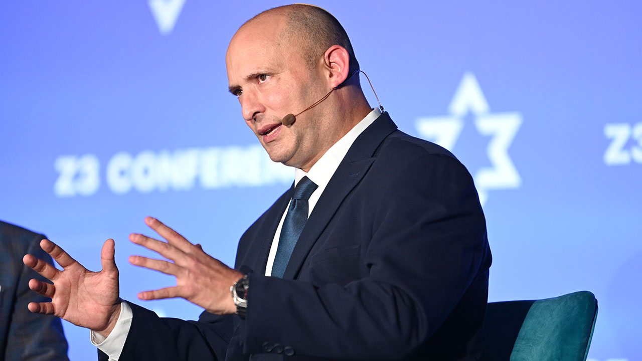 Bennett gestures as he speaks, seated on stage