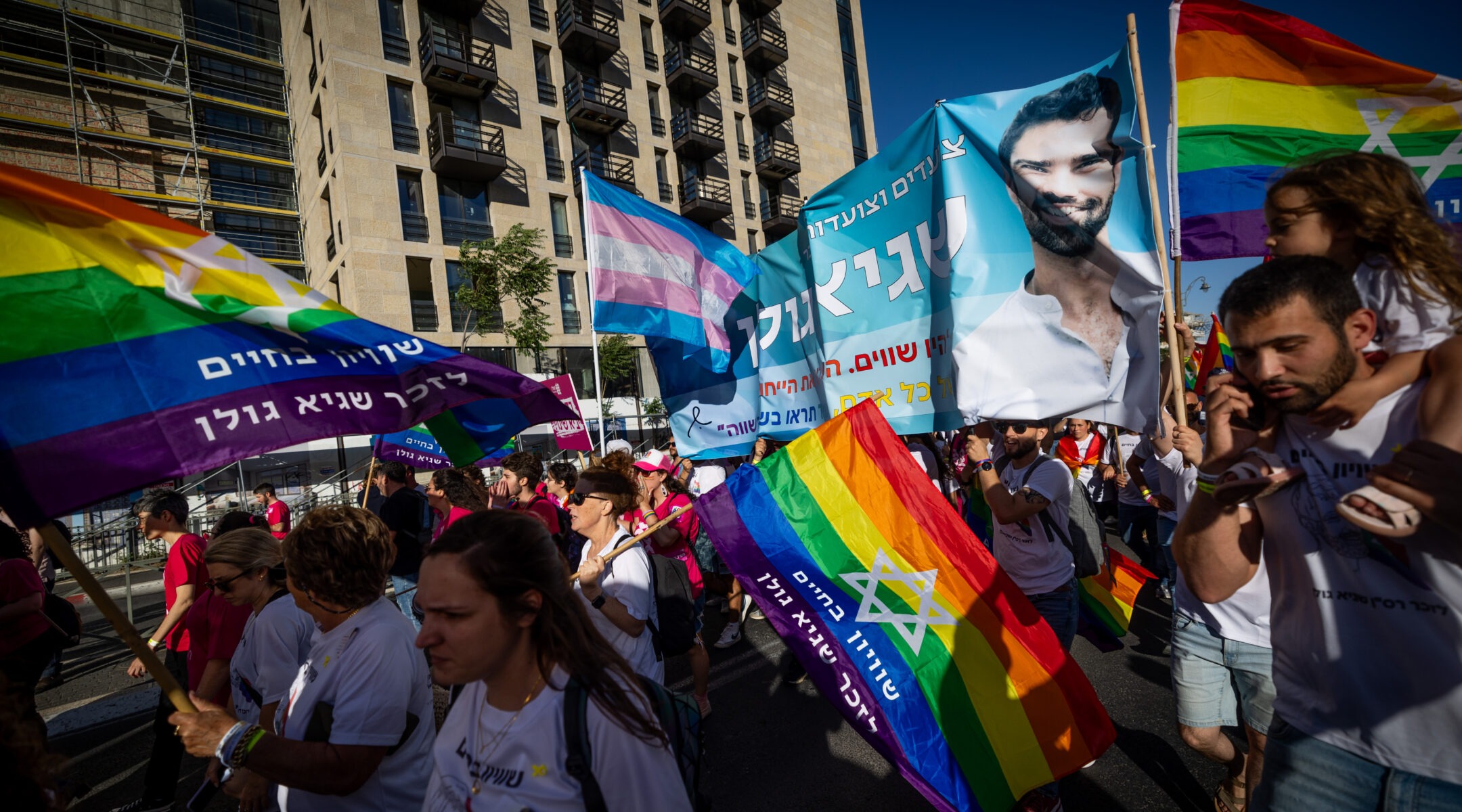 A crowd of marchers waving rainbow flags, trans flags, etc.