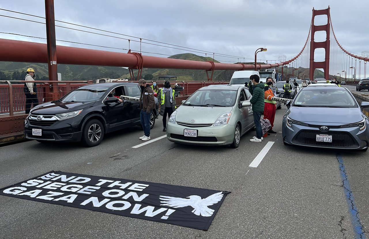 cars are stopped on the bridge in front of an "End the siege on Gaza now!" banner
