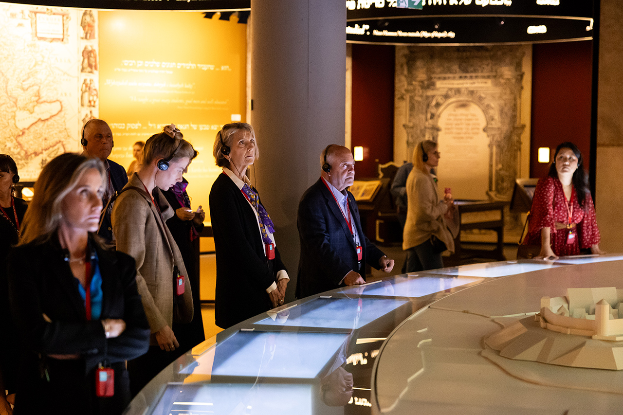 several people stand looking at museum exhibit, some wearing headphones