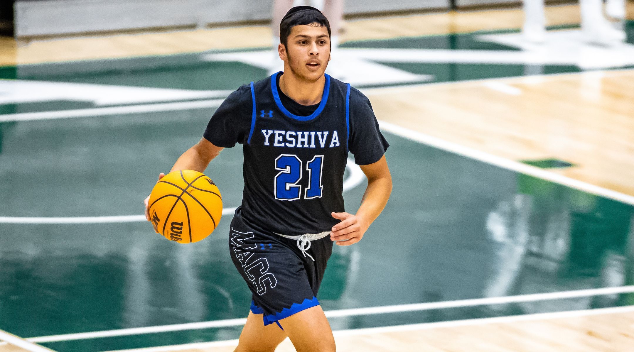 a player in a Yeshiva jersey dribbles the ball
