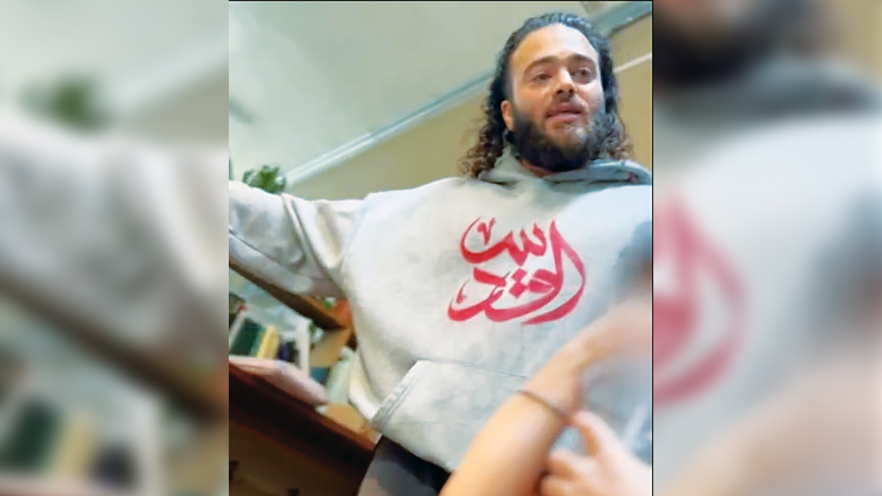 a man in a hoodie with arabic text puts his arm out in a "leave" gesture