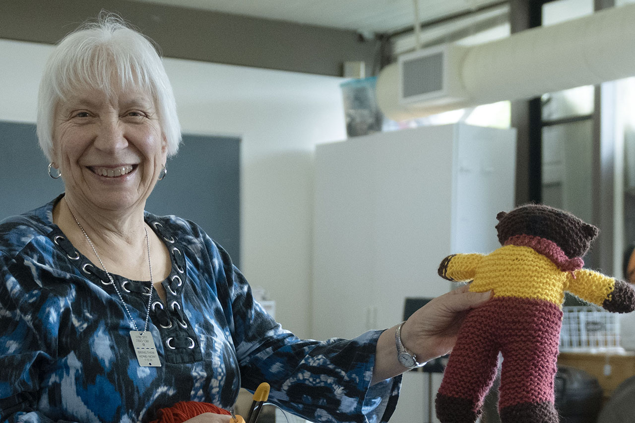 An older woman holds up a crocheted teddy bear