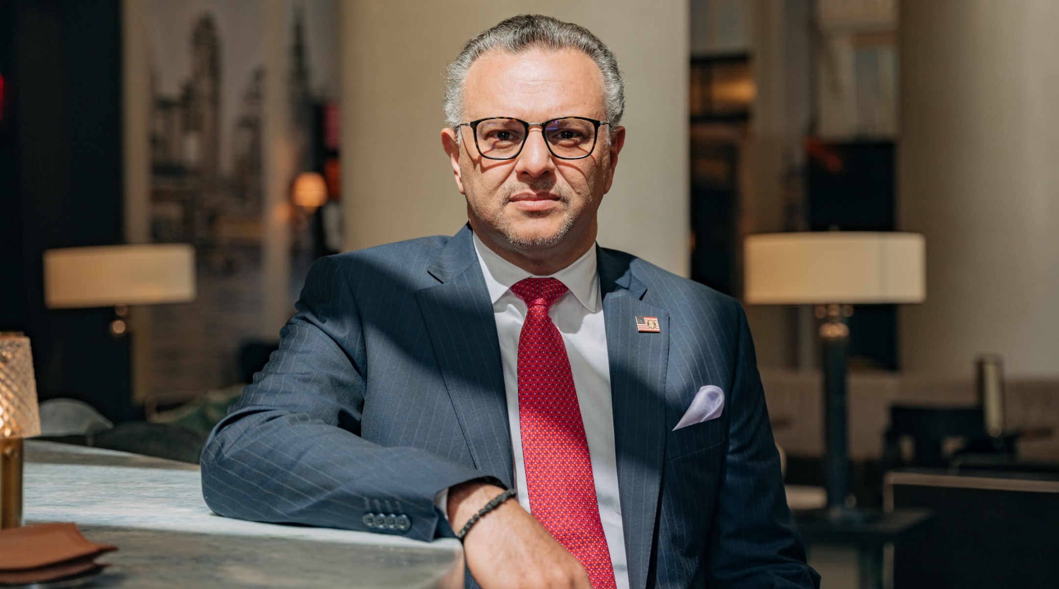 A man in a suit and glasses poses for a portrait with a neutral expression on his face