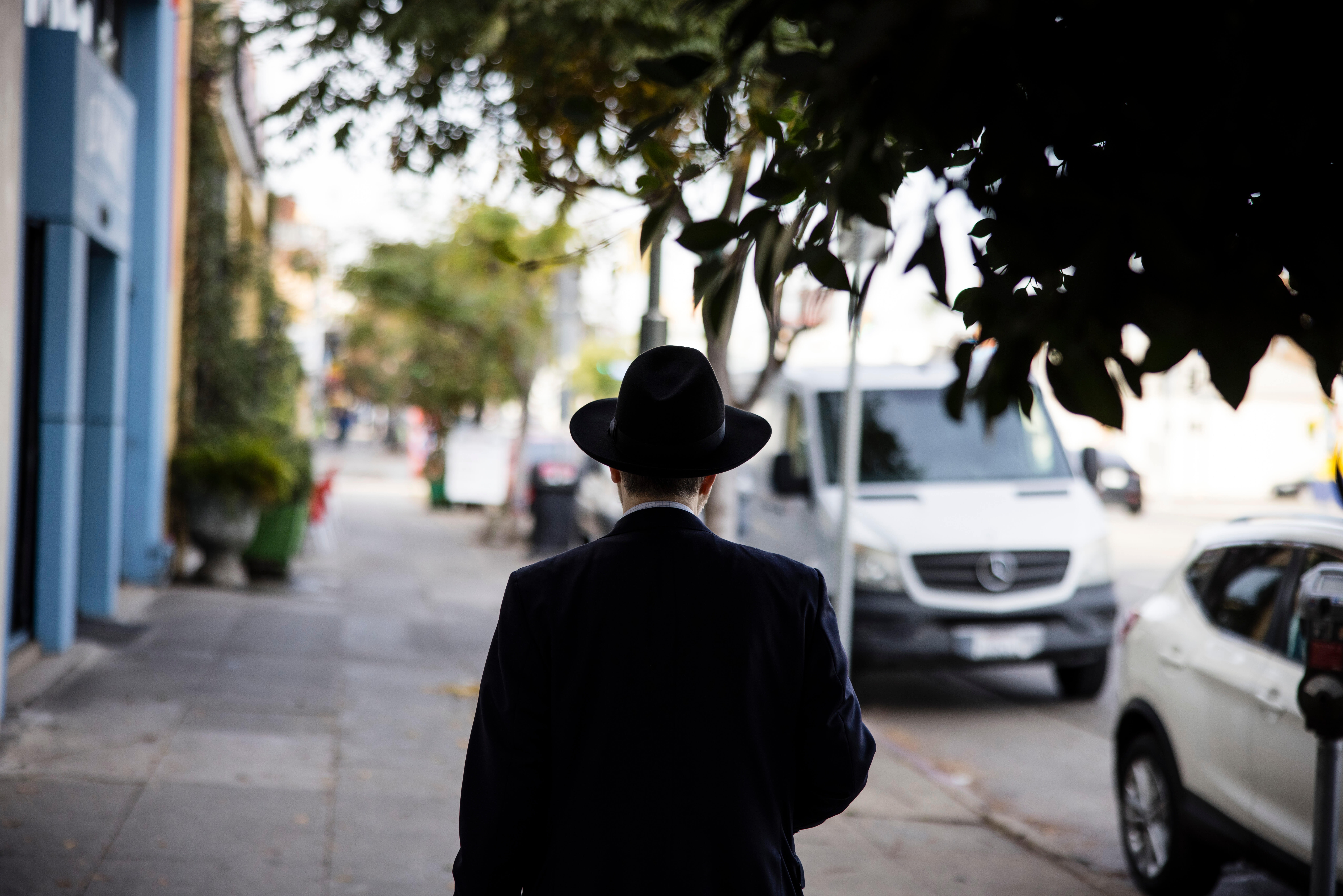 A man in a black suit and black hat seen from behind as he walks down the sidewalk