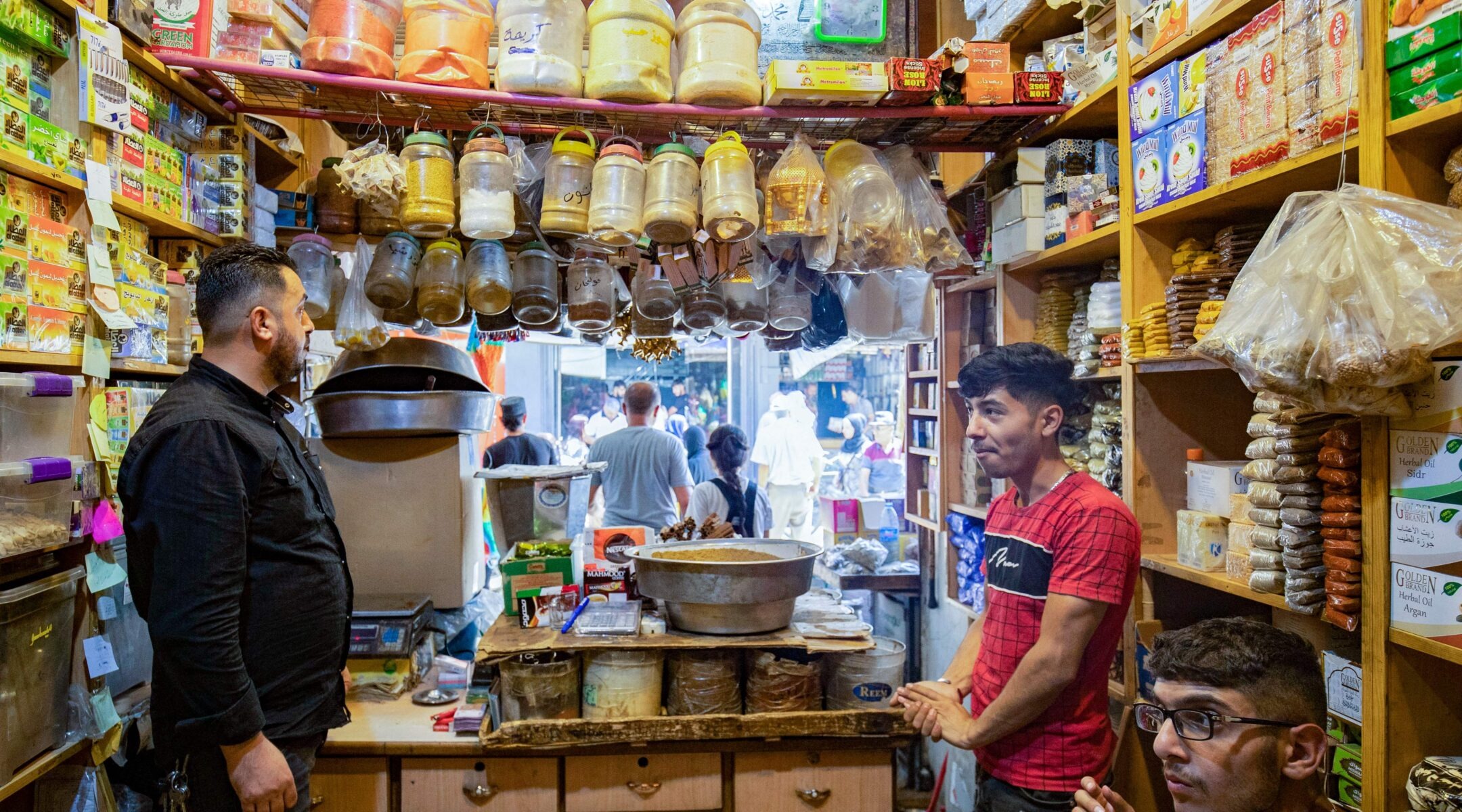 Two men stand behind the counter of a stall crowded with products