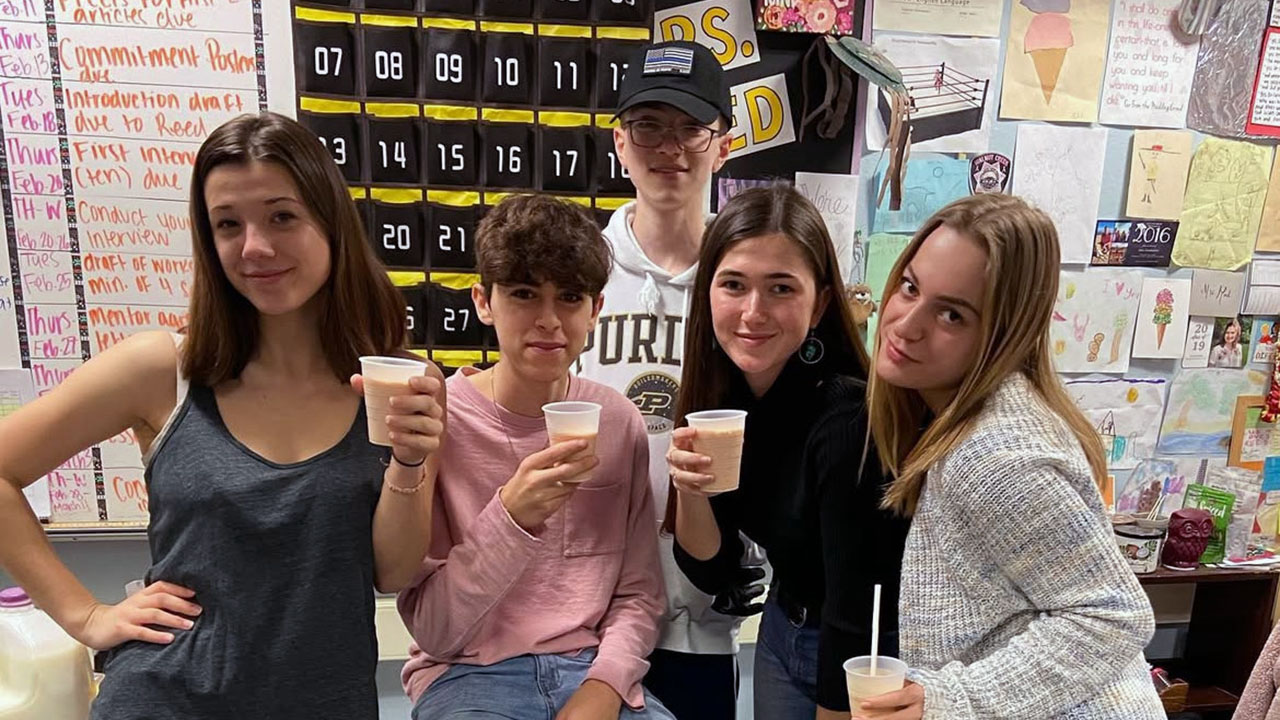 five teens - two boys and three girls - pose in a classroom