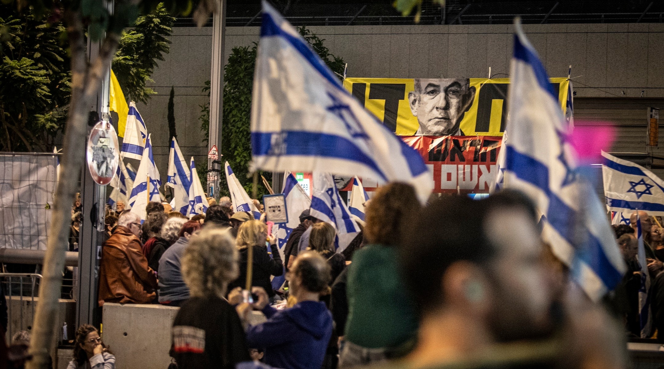 A crowd waves Israeli flags as it gathers on the street in Tel Aviv