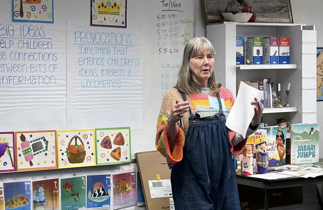 A middle-aged woman stands speaking a classroom