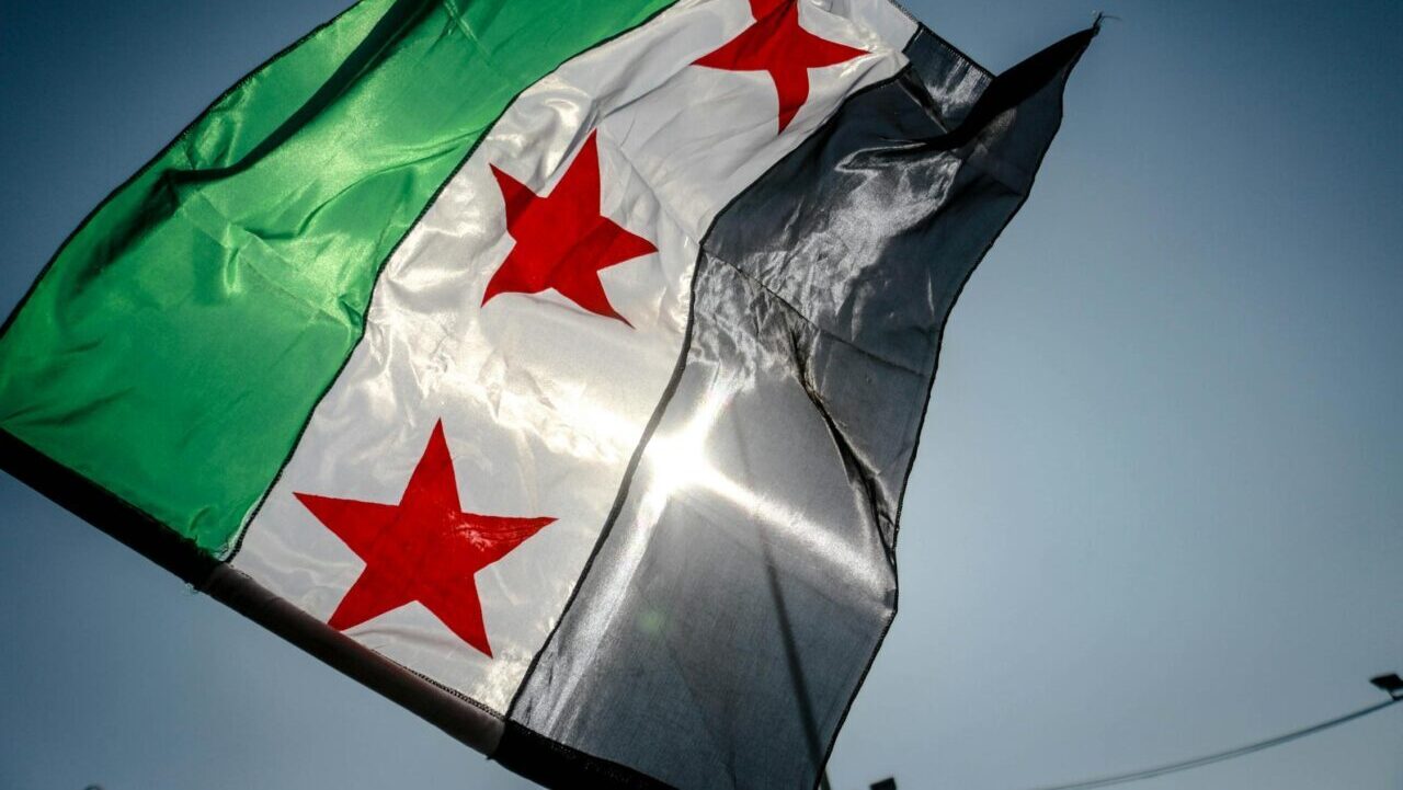a black, white and green flag with three red stars waves in the air