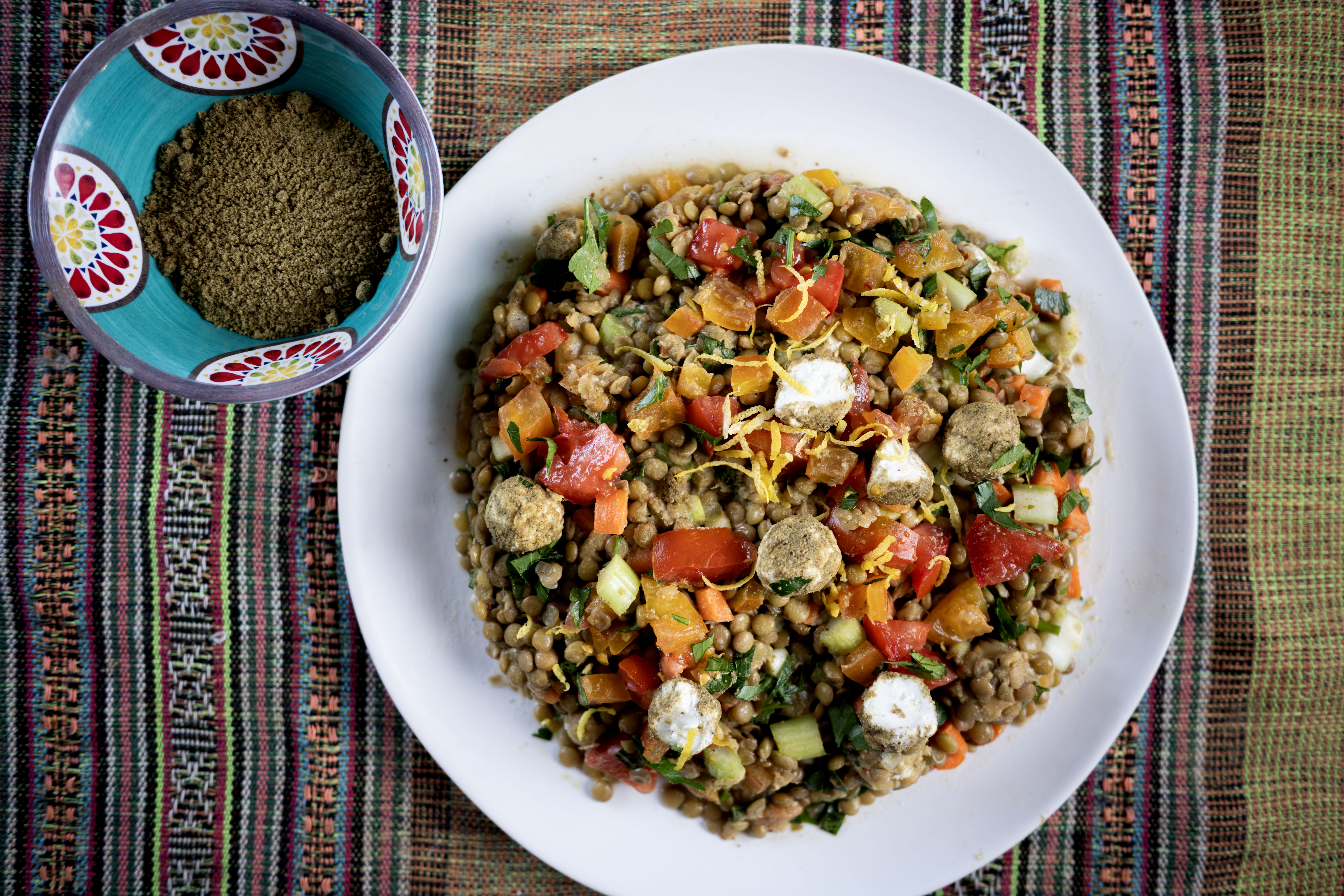 a plate of colorful salad next to a small dish of zaatar seasoning