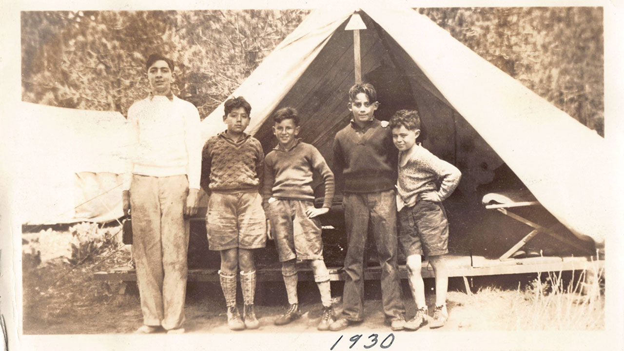 a black and white photo of five kids standing in front of a small tent