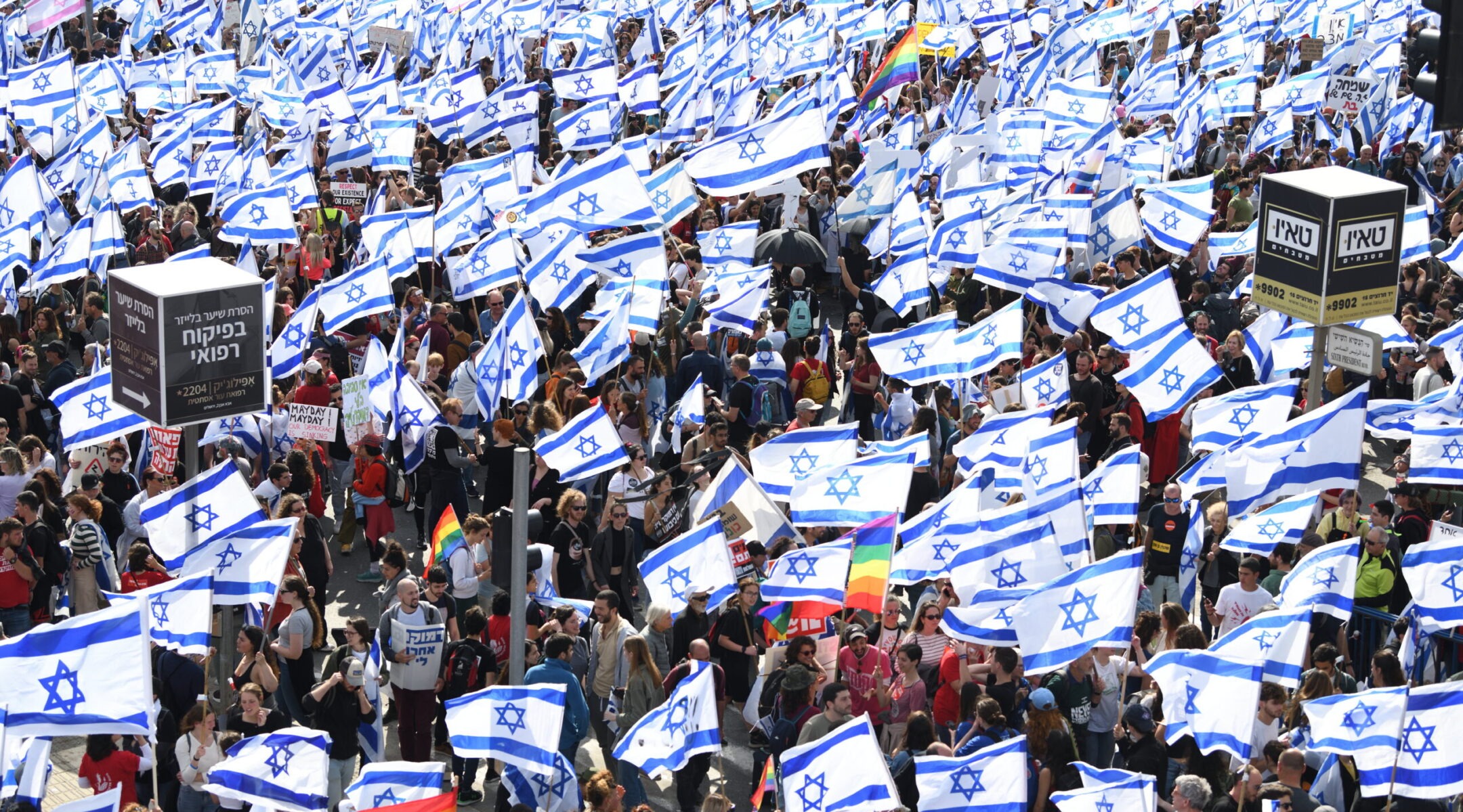 a very large crowd marches together holding many Israeli flags