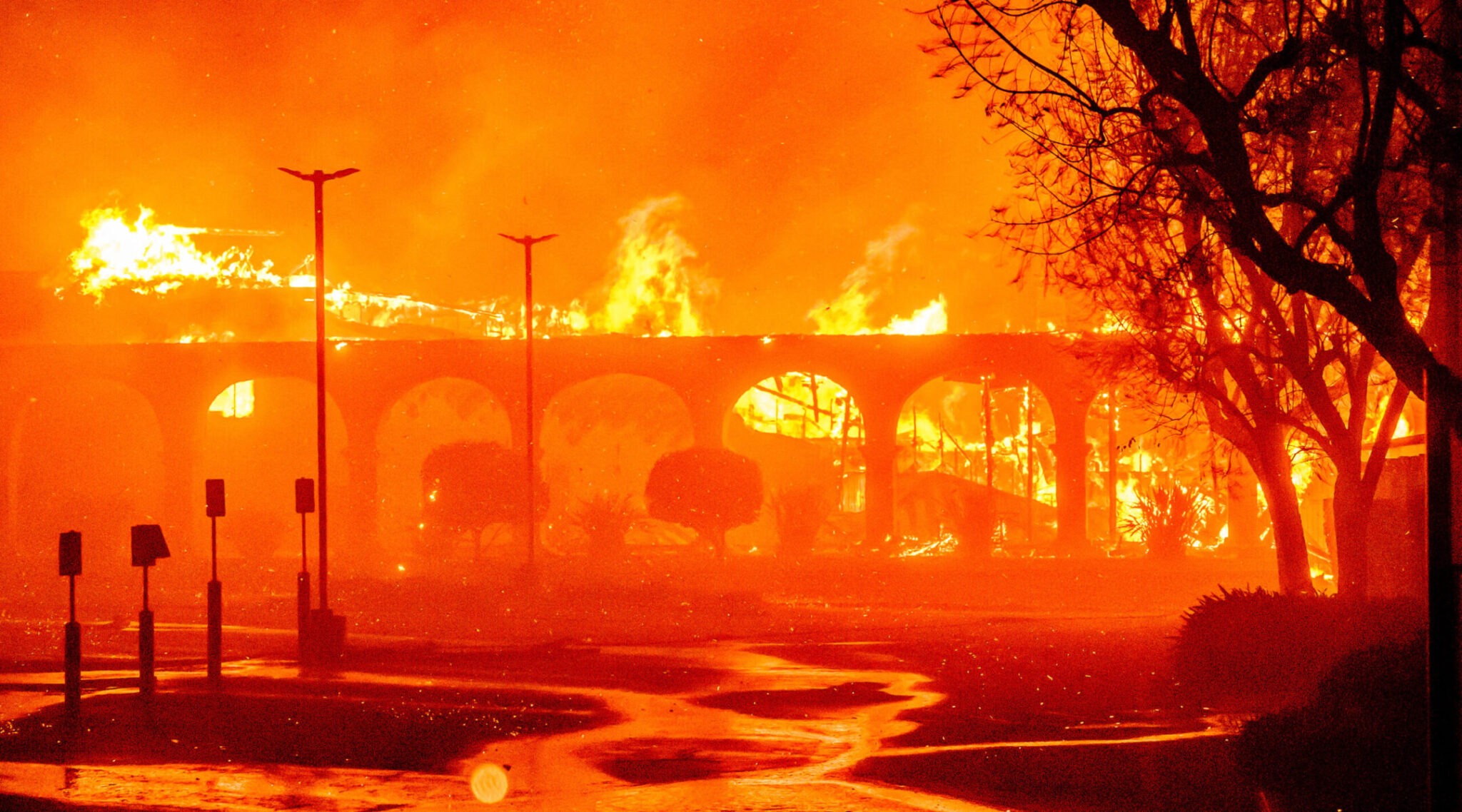 a colonnaded building with a large parking lot is engulfed in flame