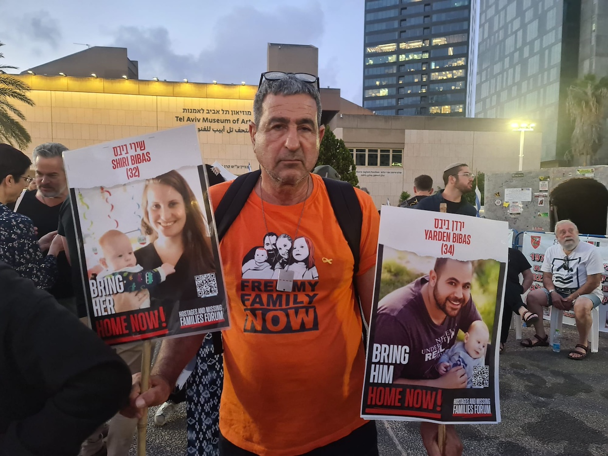 Eli Bibas holds pictures of his grandsons, who remain hostages in Gaza, during a pre-Passover rally in Tel Aviv. (Deborah Danan)