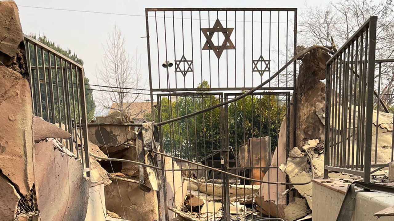 a metal gate with metal Stars of David stands amid rubble of a burned down building