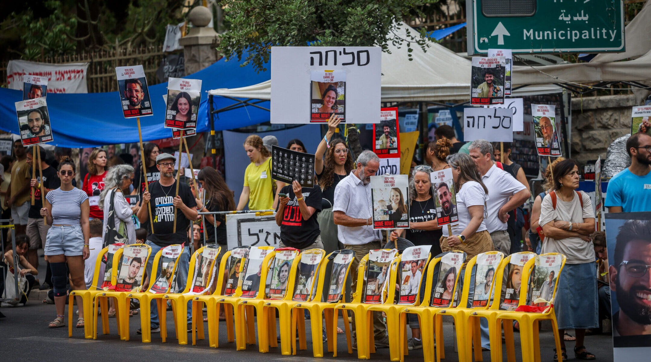 A group of protesters mill around outside with posters showing faces of the hostages