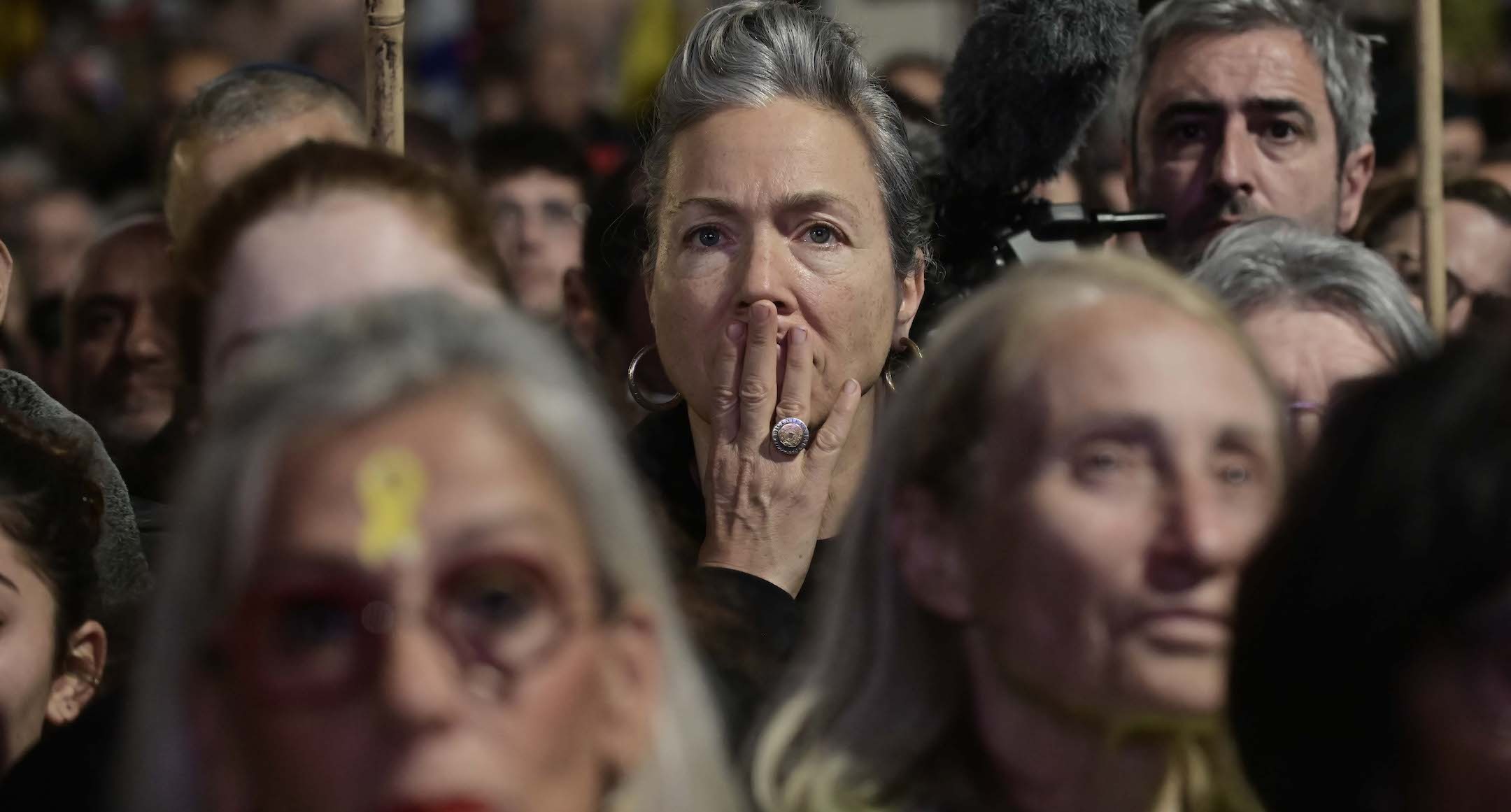 A closeup of a woman in a crowd — her hand is over her mouth as if she is gasping in shock