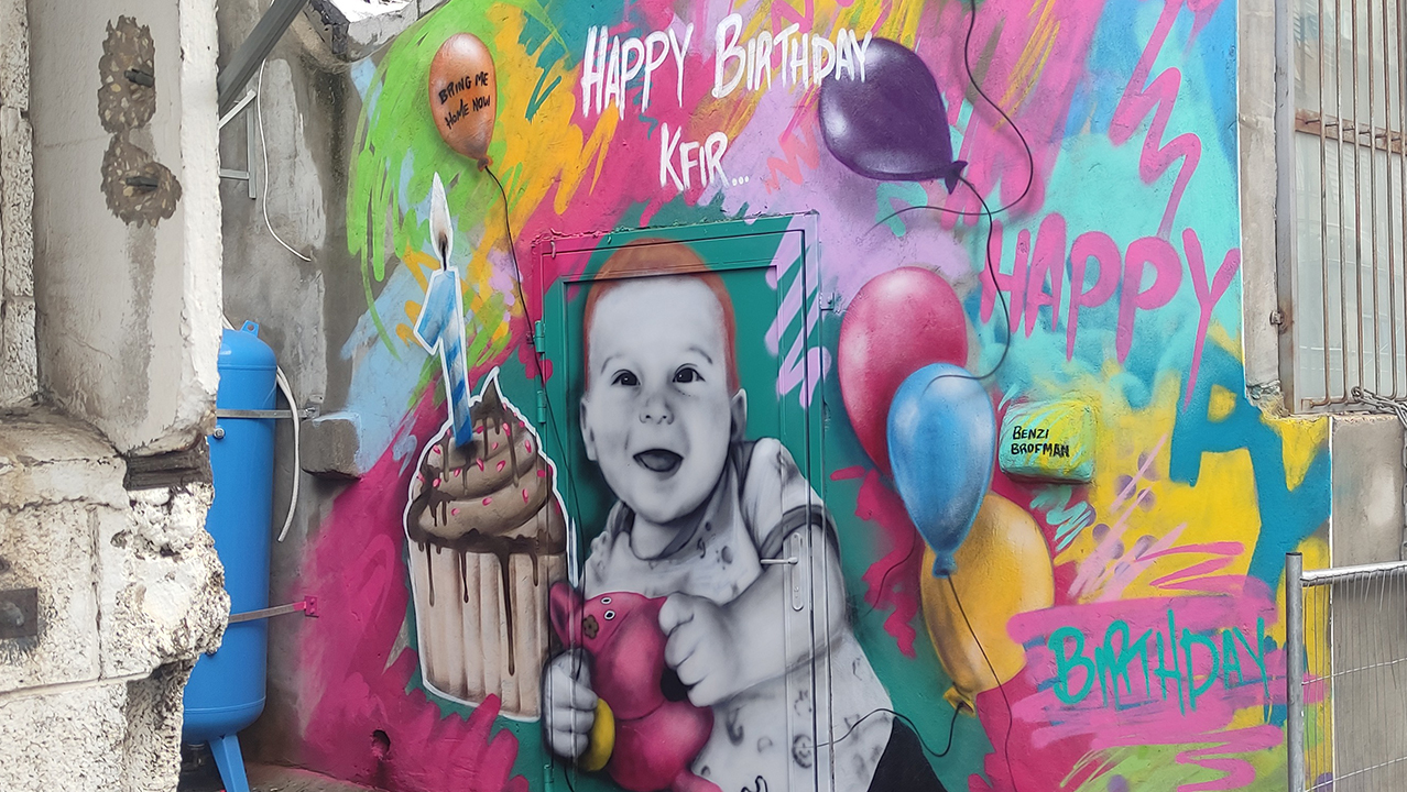 a colorful painting in an alleyway shows a happy baby surrounded by balloons and giant cupcake