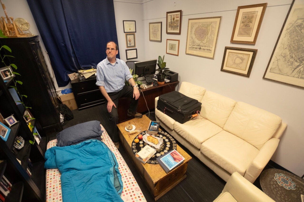 Man sits in small office with sofa and small on floor.