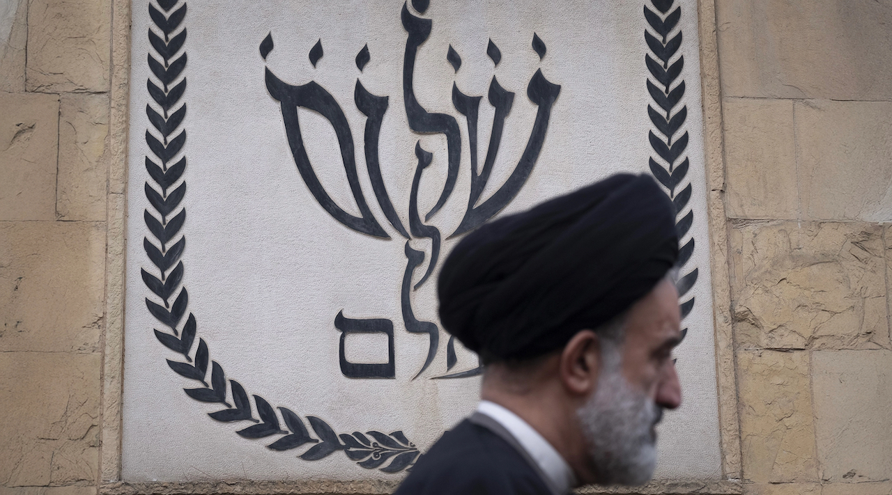 An Iranian cleric walks past a Jewish symbol of a menorah, shaped to spell the Hebrew words "shalom olam," meaning "world peace," during a ceremony commemorating the Jewish soldiers who died in the Iran-Iraq war (1980-88) at a Jewish cemetery in southern Tehran, Iran, on Feb. 6, 2025. (Morteza Nikoubazl/NurPhoto via Getty Images)