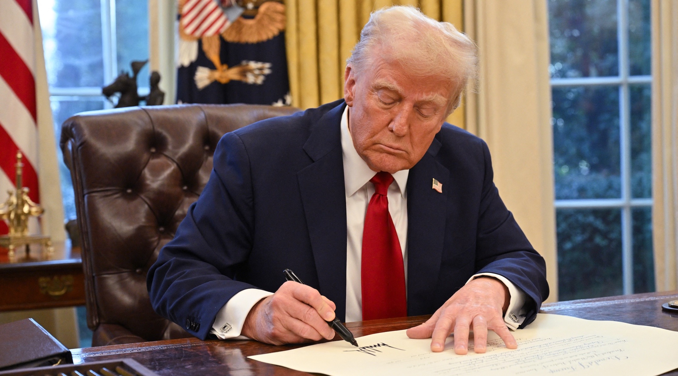 Trump signs a piece of paper on his desk