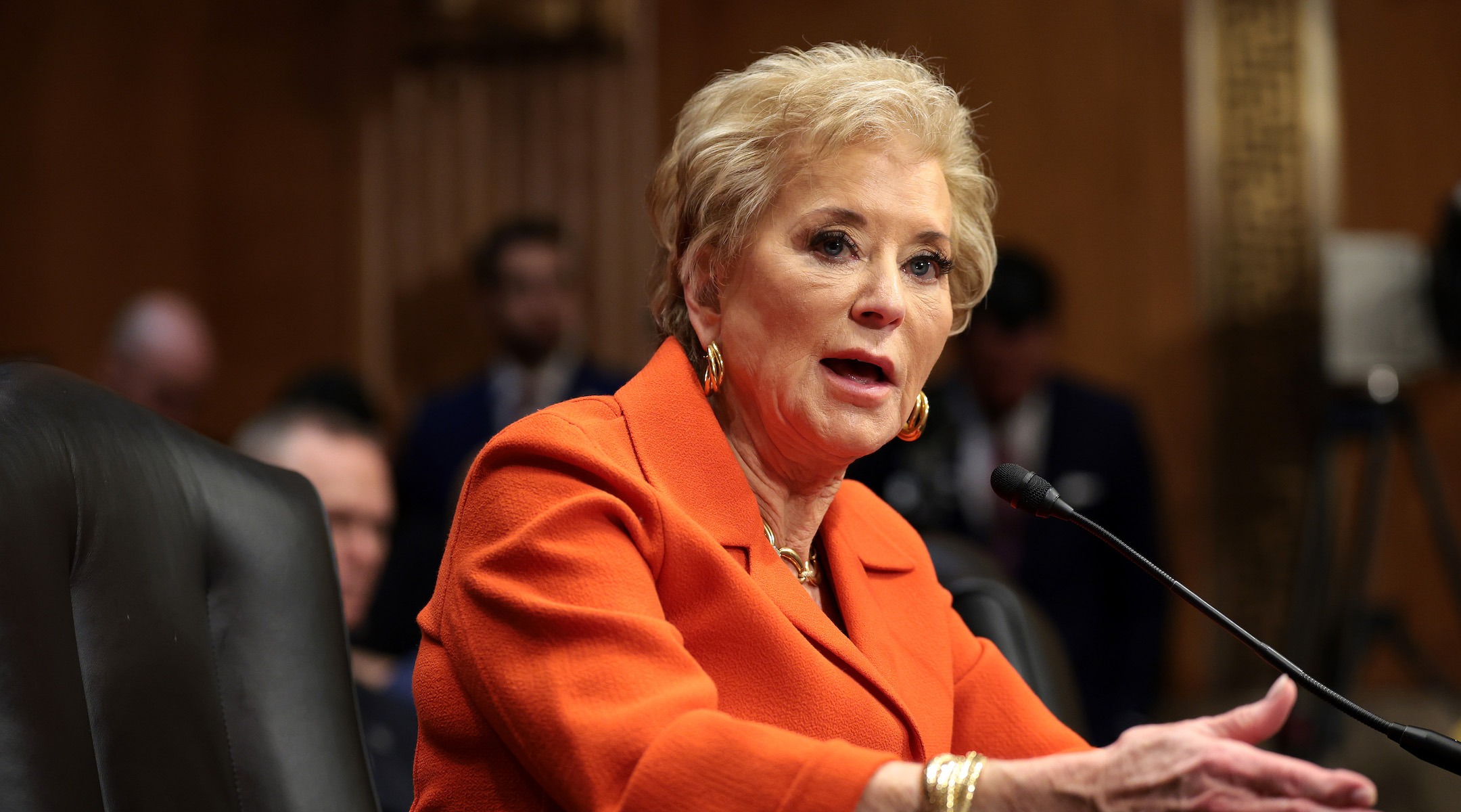 A seated older woman leans forward to speak into a microphone