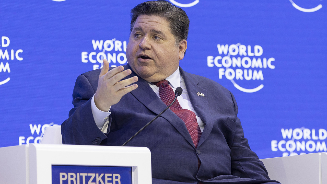 a man in a suit sits on a stage speaking into a microphone