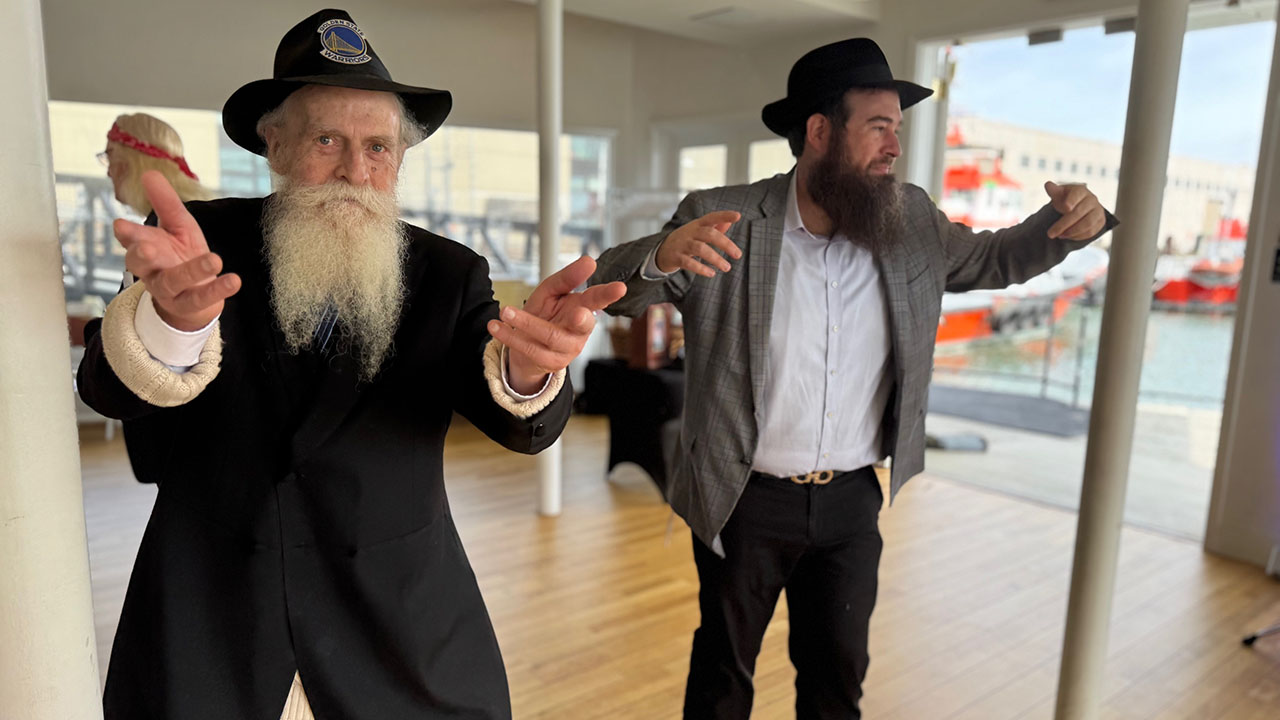 Rabbi Yosef Langer (left) dances with his son Rabbi Moshe Langer during the elder Langer’s 79th birthday onboard the Historic Klamath in San Francisco, April 6, 2025. (Sue Fishkoff)