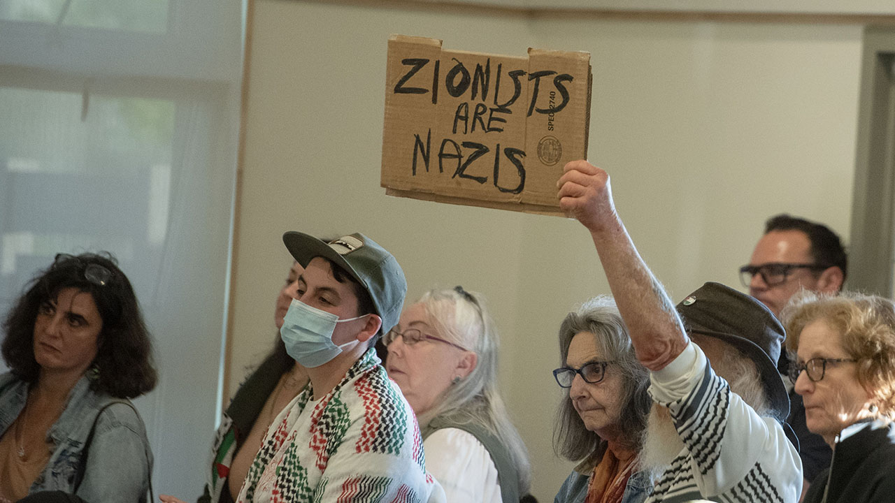 An anti-Israel activist holds a cardboard sign that reads “Zionists are Nazis” as the Berkeley City Council discusses a Gaza cease-fire resolution on April 28, 2025. (Aaron Levy-Wolins/J. Staff)