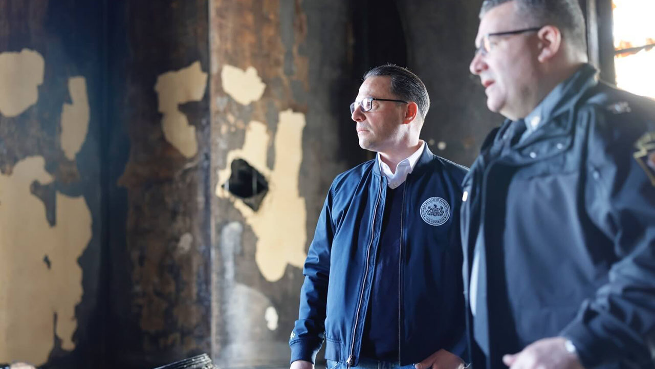 Shapiro and a police officer stand in a room with charred walls