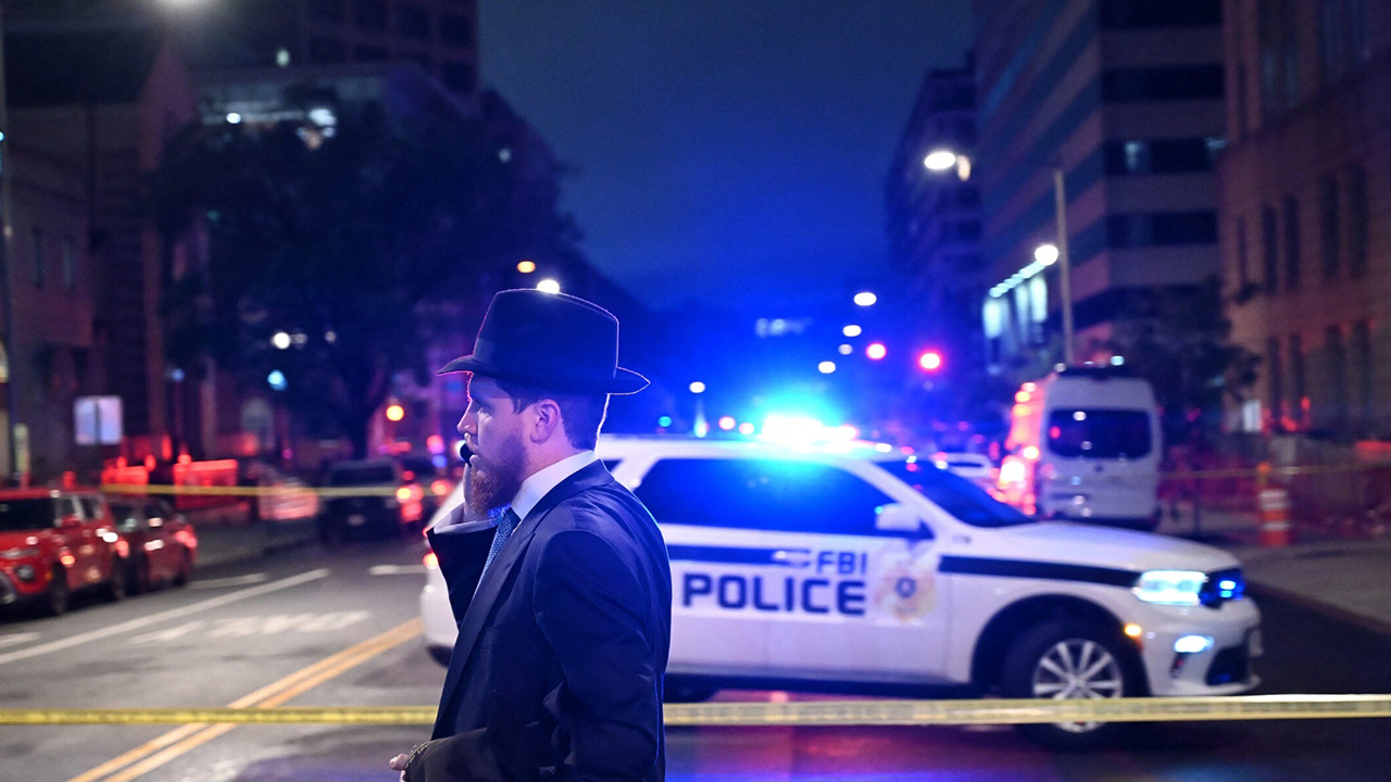 A man, standing behind police tape, talks on his cell phone outside the Capital Jewish Museum following a shooting that left two people dead, in Washington, DC, in the early hours of May 22, 2025. Two Israeli embassy staffers were killed in the shooting. (Alex Wroblewski/AFP via Getty Images)