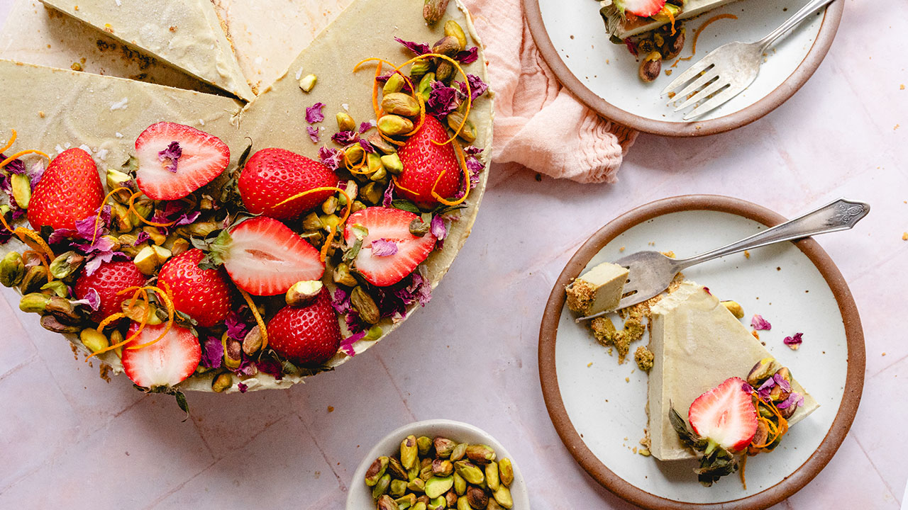 a slice of cheesecake garnished with pistachios and a strawberry sits on a plate