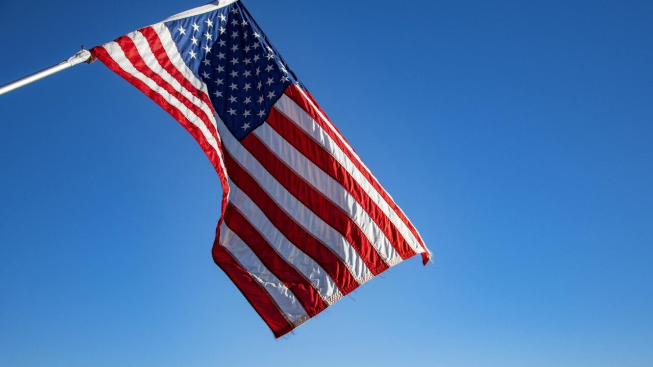 The American flag proudly waves on a flagpole against a clear blue sky, symbolizing freedom and patriotism.