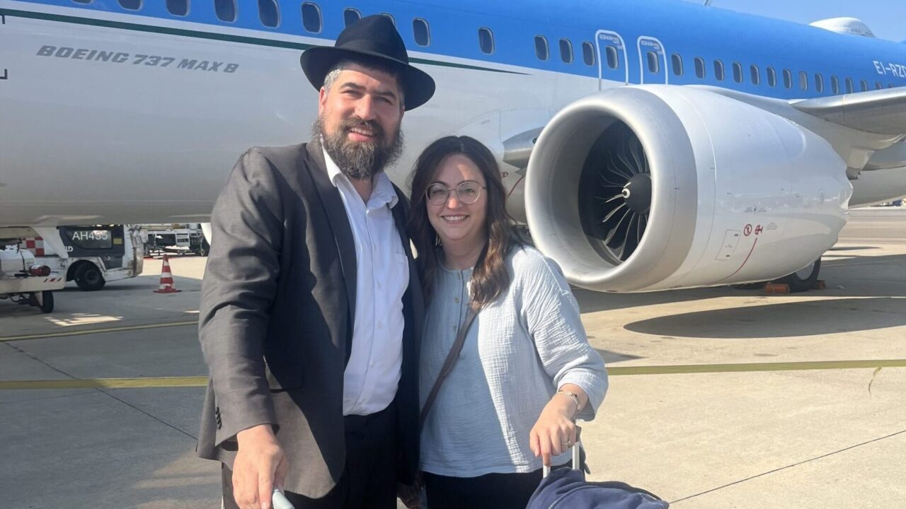 Man and woman stand with luggage in front of plane.