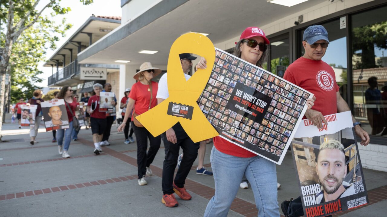 Susan Rojo Firsty holds a yellow ribbon cardboard cutout and a poster of the hostages during a Run for Their Lives event in Los Gatos on June 8. (Aaron Levy-Wolins/J. Staff)