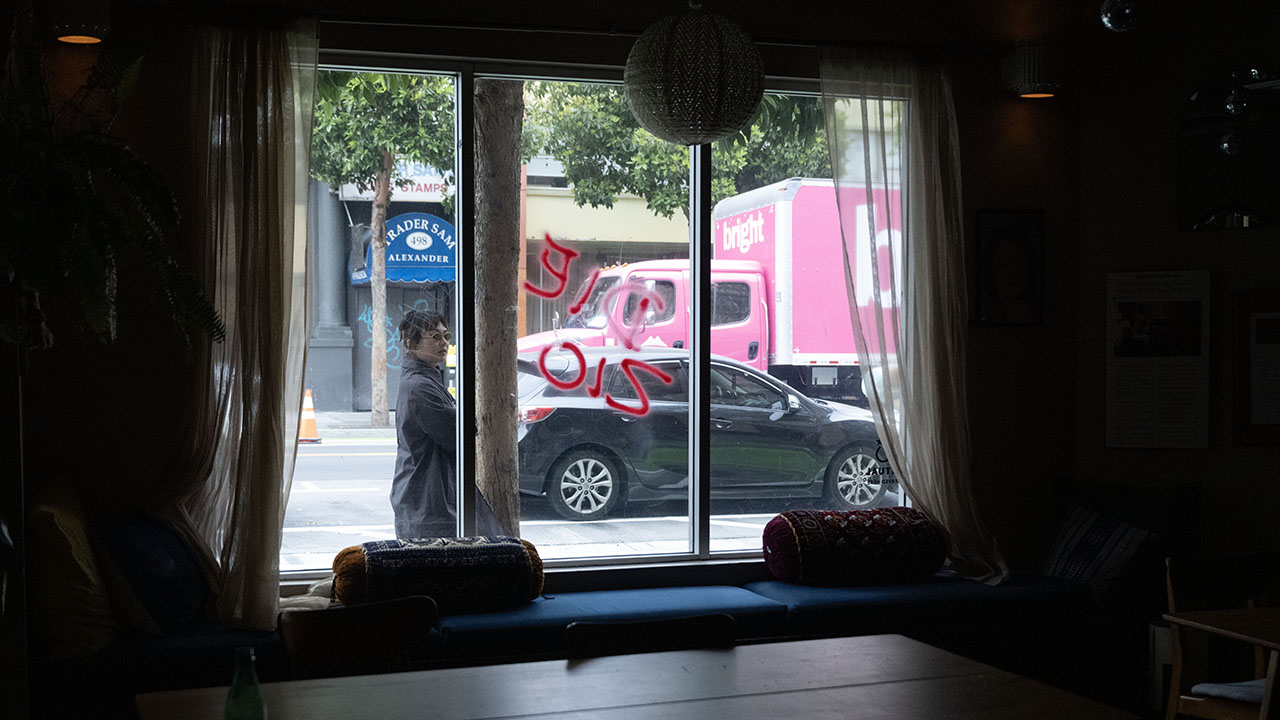 A passerby looks at a window with the words “Die Zio” spray-painted on it at Jewish-owned cafe and civic engagement space Manny’s in San Francisco, June 10, 2025. (Aaron Levy-Wolins/J. Staff)