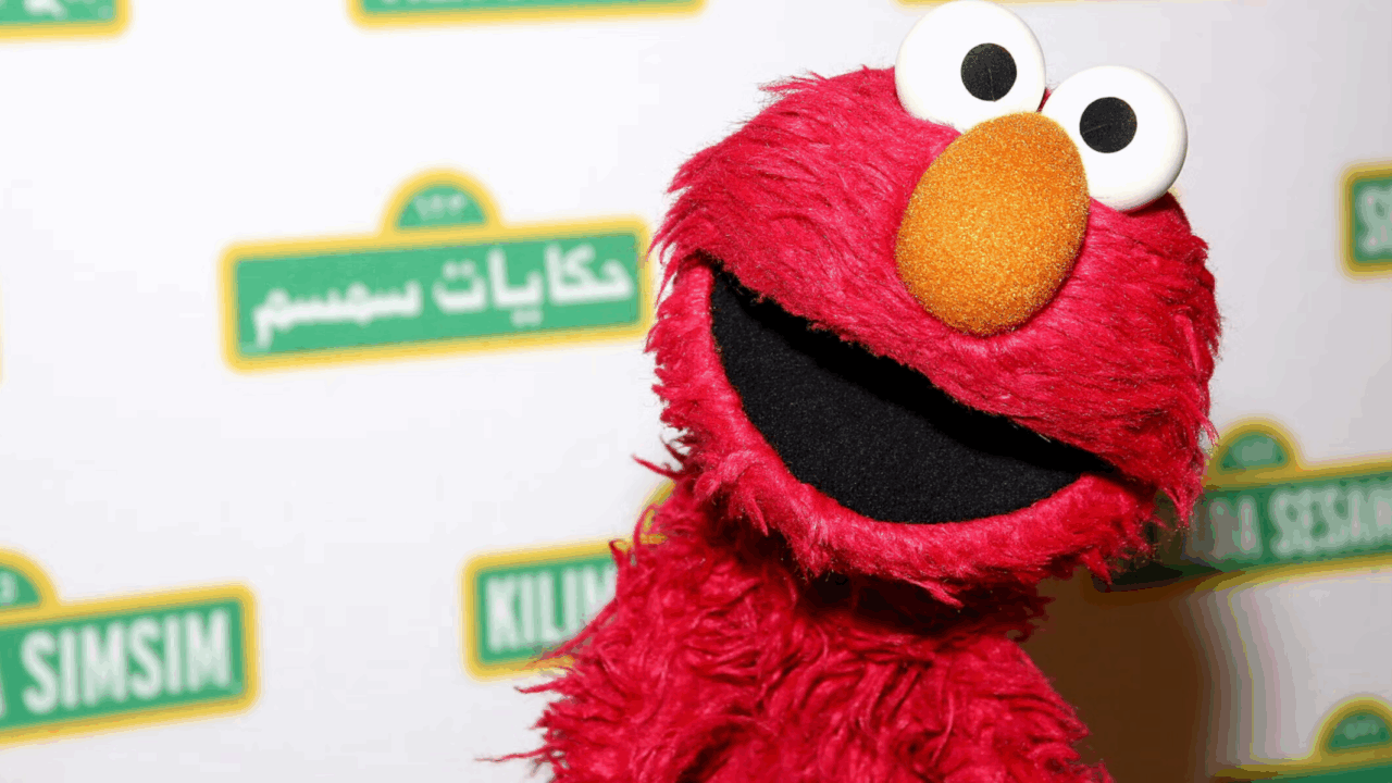 Elmo puppet in front of Sesame Street background