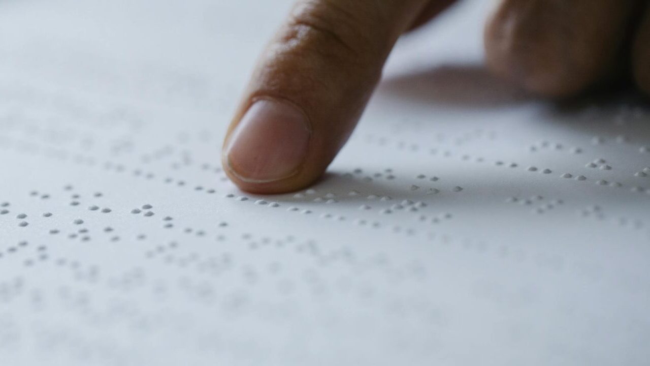 Close-up of a finger reading braille text on a textured white paper, emphasizing touch.