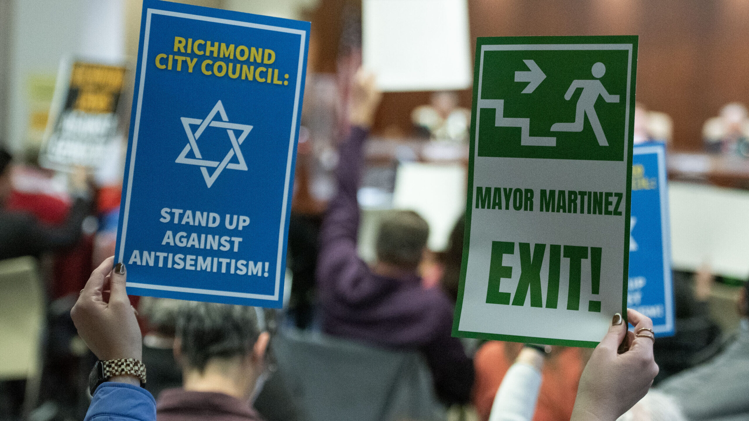 An opponent of Richmond Mayor Eduardo Martinez holds up signs calling for his resignation during a Richmond City Council meeting, Jan. 6, 2026. (Aaron Levy-Wolins/J. Staff)