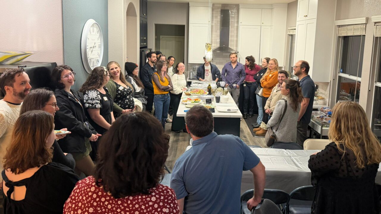 Group of people stand in a circle in a kitchen