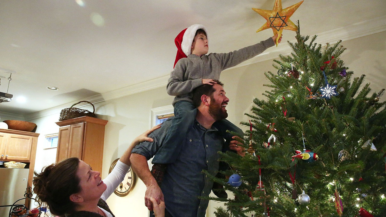 Karolyn Feeks Maws, who is Christian, her Jewish husband, Tony Maws, and their 8-year-old son Charlie Maws, decorate their Christmas tree with a homemade Star of David. (Pat Greenhouse/The Boston Globe via Getty Images)