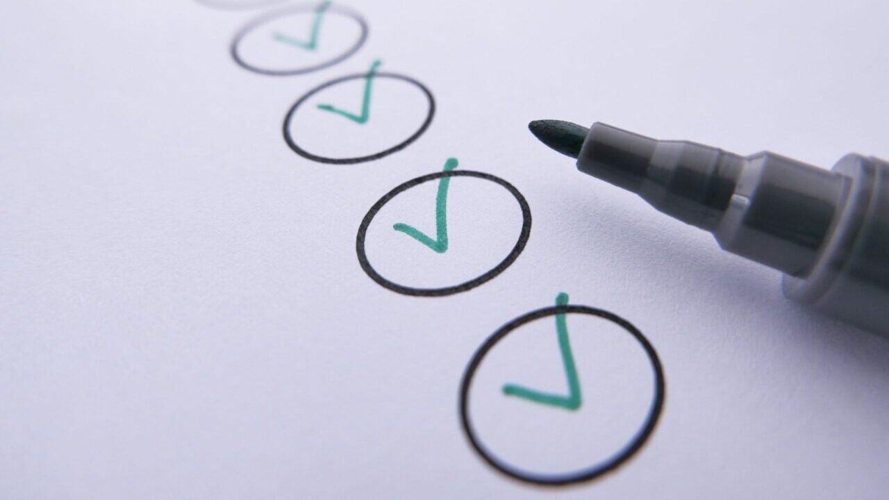 Close-up of a checklist with green checkmarks on white paper using a marker.